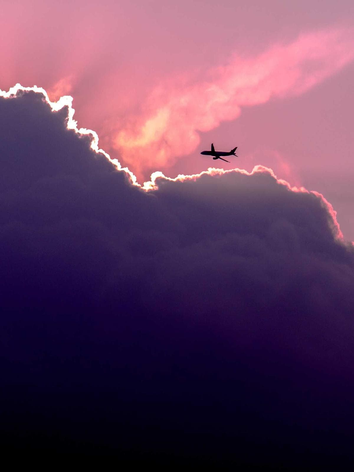 Airplane crossing a purple sky above the clouds